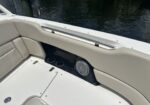 White boat seating with beige cushions, a stainless steel grab rail, cup holders, and a built-in speaker; water visible outside.