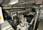 Marine engine room with a large diesel engine, hoses, and metal piping in a tight workspace in a boat or ship.