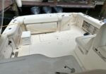White boat deck with seating, cooler, and yellow power cord laid across the cockpit near the docked sterns.