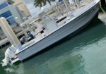 White fishing/pleasure boat docked at a marina, with twin Suzuki outboard motors and a canopy, beside modern buildings.
