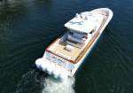 Aerial view of a large white motor yacht cruising through blue-green water, seen from above with a sun deck and multiple outboard engines at the stern.