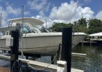 White motorboat on a lift at a marina, with blue sky and palm trees in the background.