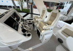 White yacht cockpit with two cream leather captain chairs and a chrome steering wheel; dashboard with electronics visible on the left side.