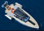 A luxury motorboat viewed from above on deep blue sea, showing a spacious deck with tan seating and a dark cockpit area