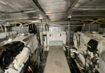 Cramped engine room with two large white marine diesel engines on either side, metal walkway, and central control cabinet.