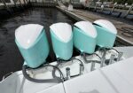 Four turquoise Yamaha 350 outboard motors mounted on the stern of a white boat at a wooden dock.