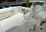 White boat cockpit with captain's chair, rod storage, and built-in storage; yellow cord runs across the deck, twin outboard motors visible aft.