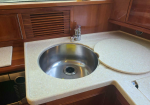 Round stainless steel sink set in a beige speckled countertop with a chrome faucet and a circular cutting-board cover nearby on the right.