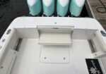 White boat at a dock with four teal outboard engines mounted at the stern and a white interior deck nearby.