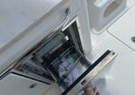 Pull-out cooler drawer on a boat with water bottles and a towel inside, partially extended by a hand.