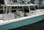 White and teal powerboat docked at a marina, showing a center console, multiple seating stations, and a tall overhead framework (tower).