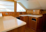 Wood-paneled galley kitchen with white countertops, sink, and built-in appliances under a sloped ceiling.