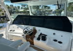 Yacht helm station with three large navigation screens, chrome steering wheel, and control levers on a white glossy dashboard.