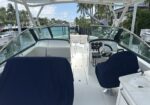 White motorboat cockpit with steering wheel and gauges, navy-covered seats, dockside canal with palm trees in the background
