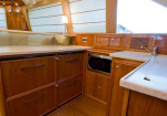 Wooden galley kitchen on a boat with countertops, sink, microwave, and storage cabinets nearby.
