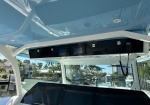 Boat cockpit helm with two Garmin displays and a radio handset, under a tinted hardtop, overlooking a canal with palm trees and docked boats.