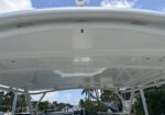 White boat hardtop above the cockpit with clear blue sky; canal and palm trees visible in background.