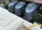 Three Yamaha V8 outboard motors mounted on the stern of a white boat docked at a wooden pier. IMG shows a trio of gray engine covers labeled V8 and Yamaha, with a yellow hose in the foreground.