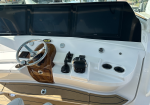 Boat cockpit with three large Garmin screens, polished steering wheel, and wood-accent console workspace.