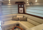 Cream leather curved sectional sofa with pillows in a yacht cabin, wood paneling, and large horizontal blinds over windows; framed artwork on the wall.