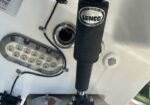 Close-up of a Lenco Marine transom mount with a black hydraulic actuator, attached to a boat's stern and a small leaf resting on a metal plate nearby.