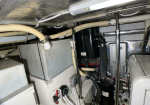 Mechanical room with white utility cabinets, insulated ducts, and a black vertical component among silver pipes and wiring.