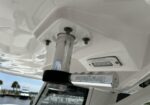 Close-up of a boat ceiling showing a chrome pedestal rail mount secured with bolts and a nearby rectangular cockpit light; Everglades-branded rod holder attached nearby.