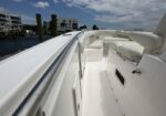Top deck of a white luxury motorboat with cushioned seating and stainless railing, dockside harbor in the distance under a blue sky.