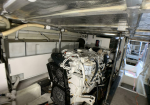 Industrial engine room with a large white generator engine, hoses and metal piping surrounding it, under a metallic ceiling.
