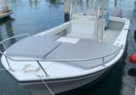 White motorboat with gray cushioned bow seating docked at a marina, tied to a dock with ropes.