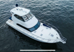 A white motor yacht viewed from above, sailing on dark blue water with a spacious bow deck and railings visible on the side.