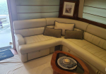 Cream-colored curved leather sofa with three beige throw pillows in a boat cabin, with a wooden coffee table and remote nearby.