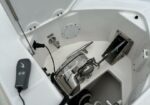 Deck of a boat with an electric anchor windlass and control handset resting on the hatch ledge; ropes and metal fittings nearby.