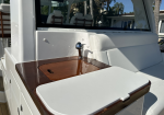 Back deck of a white luxury boat with a polished wooden table, chrome faucet, and white cushioned seating.