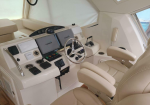 Boat cockpit with beige captain's chair, chrome steering wheel, and multiple Garmin screens at the helm.