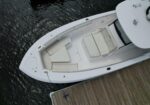 Top-down view of a white motorboat docked at a wooden pier, showcasing cream-colored cushioned seating and deck layout on the bow and cockpit areas.