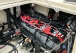 Boat engine compartment showing a dense battery bank with red/black cables, terminal clamps, and assorted wiring and fuses surrounding sturdy components.