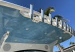 Close-up of a boat’s white hardtop with chrome rod holders, blue glass canopy, and palm trees in a clear blue sky.