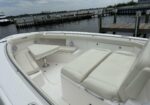 White boat cockpit with a small rectangular table and cushioned seating, dock and water in the background.