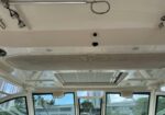 Ceiling of a boat cabin with a circular loop, metal rod, and vented panel; windows show buildings outside.