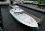 White sport fishing boat moored at a wooden marina dock, with a teal hull and upper radar arch.