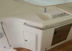 White boat galley counter with small sink, chrome faucet, built-in drainboard, and safety grab rails along the edge adjacent to a wooden cabinet door panel.