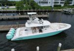 White powerboat with a teal hull docked at a wooden marina, four teal outboard motors at the stern.