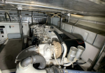 Industrial diesel engine in a dim engine room with hoses, pipes, and a control panel visible in the background (informative image of machinery).