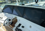 Boat cockpit with three Garmin displays behind a wooden helm panel and chrome steering wheel, dock and water outside