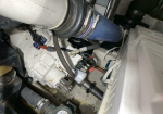View inside an engine compartment showing a large blue duct, hoses, clamps, and a white gearbox with wiring.