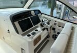 White boat cockpit with a chrome steering wheel, multiple screens, and control panels; dock and water visible through the windshield outside the helm.