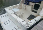 Rear cockpit of white motorboat with built‑in seating and a small hexagonal table under a blue canopy.