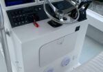 Boat helm with chrome steering wheel, black control panel, and throttle lever on a white console; red safety lanyard attached.