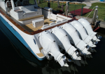 White luxury motorboat docked at a marina, showing five large white outboard engines at the stern and teak decking.